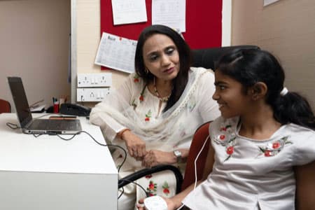 A Shaba audiologist sits with a young patient beside a laptop during a fitting