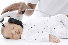 A sleeping newborn wearing small headphones during a hearing screen