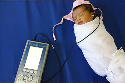 A sleeping newborn, swaddled, during a hearing screen with a handheld screener