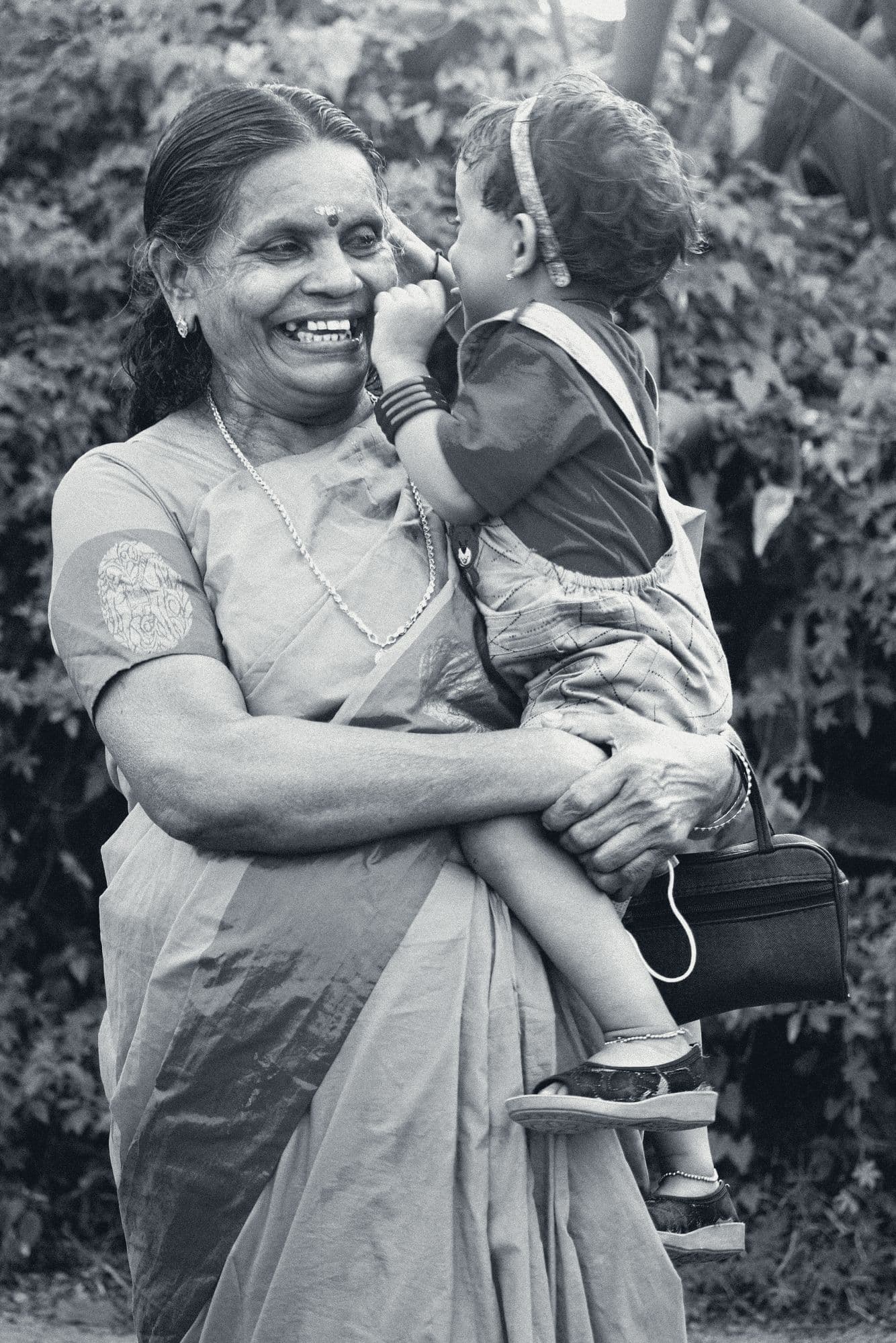 A grandmother laughs as the small child in her arms whispers into her ear