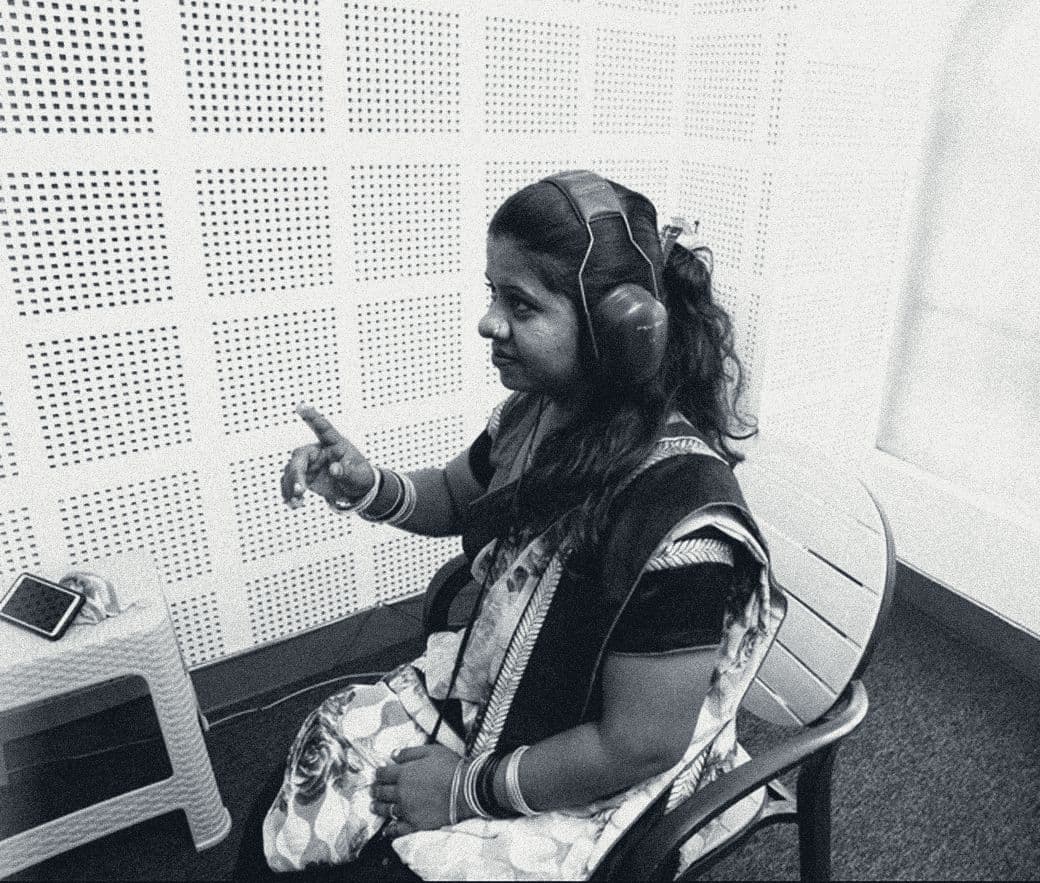 A patient wearing headphones raises her hand to signal a tone inside Shaba’s sound-treated audiometry room