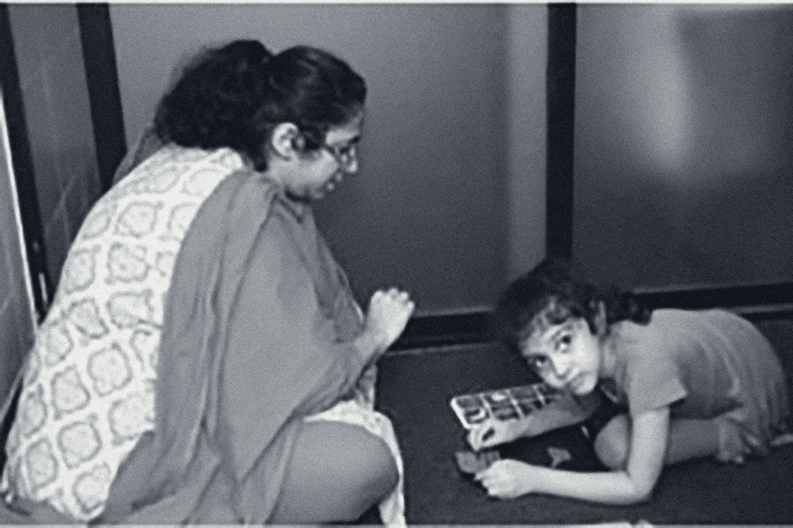 A therapist kneels beside a young girl who looks up from a picture puzzle on the floor during a session at Shaba